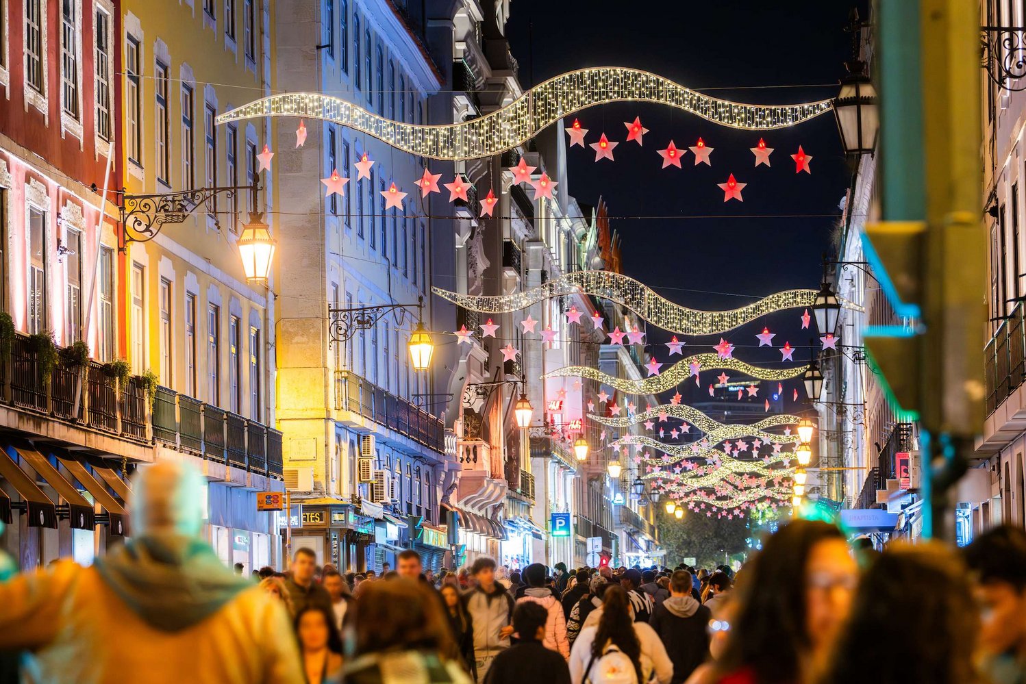 Iluminações de Natal à noite numa rua do centro de Lisboa, com pessoas a passear