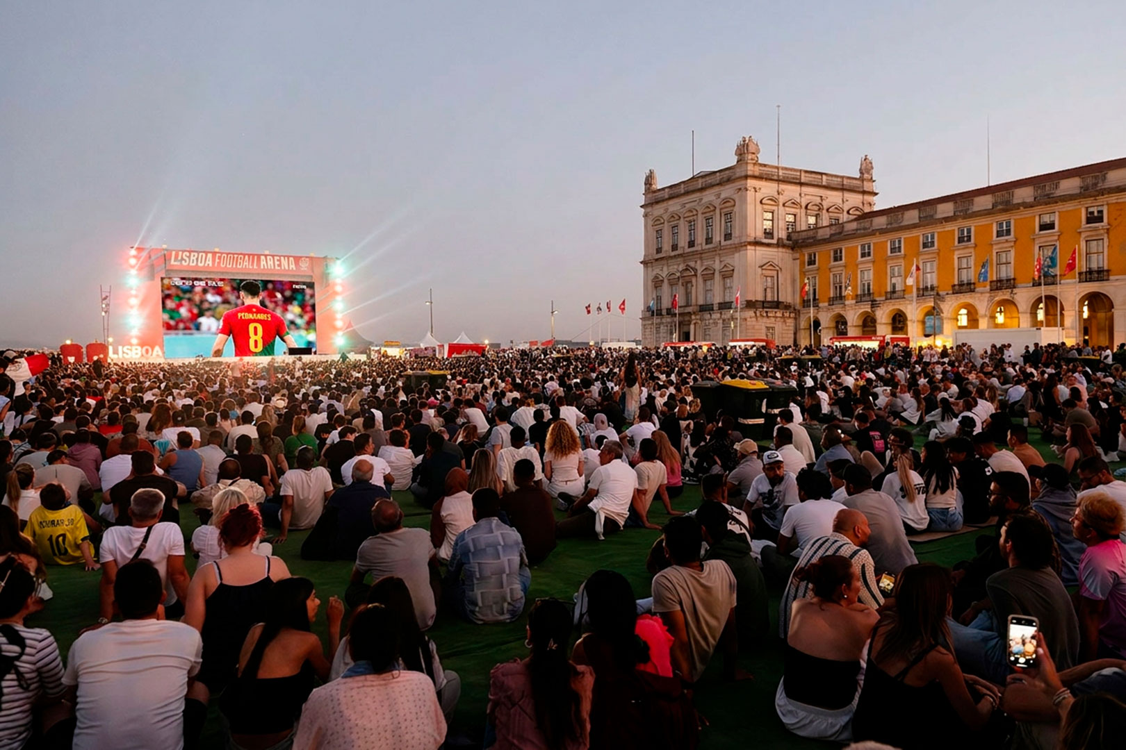 pessoas sentadas no relvado sintético a ver o jogo num ecrã gigante